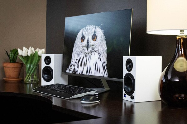 Lifestyle image of the M series white speaker next to a computer monitor
